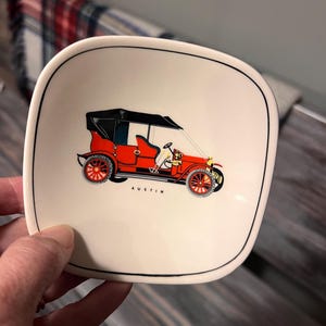 May include: A square, off-white ceramic dish with a black rim. The dish features a colourful illustration of a vintage red car with black accents. The word "AUSTIN" is printed below the car.