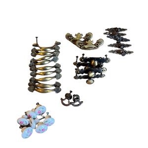May include: Assortment of vintage cabinet hardware, including brass drawer pulls, ornate metal pulls, and porcelain knobs with floral designs.