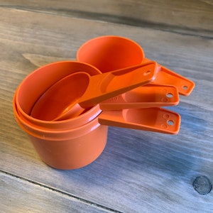 Könnte beinhalten: Ein Satz mit vier orangefarbenen Messbechern aus Kunststoff. Die Becher sind ineinander verschachtelt und haben Griffe.