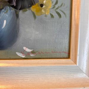 Pu&ograve; includere: Dipinto di natura morta floreale incorniciato. L'opera presenta un vaso blu pieno di fiori viola e gialli. Il dipinto &egrave; ambientato su uno sfondo azzurro ed &egrave; racchiuso in una cornice bianca e color legno.