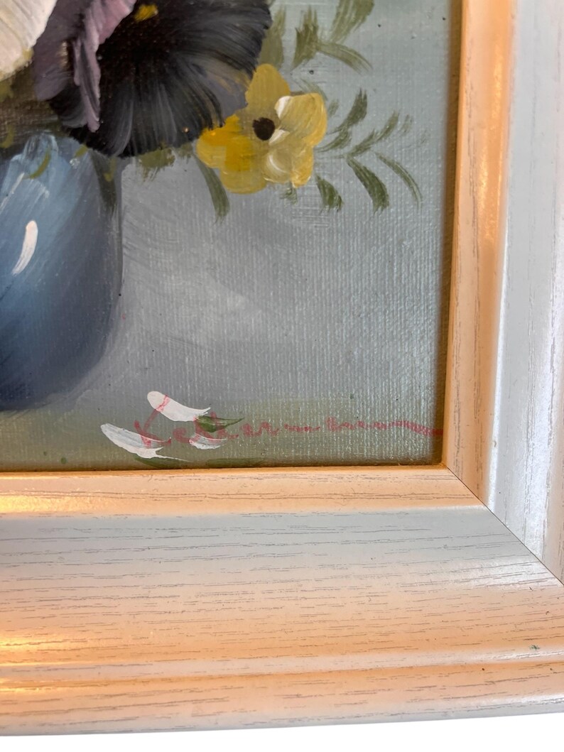 Pu&ograve; includere: Dipinto di natura morta floreale incorniciato. L'opera presenta un vaso blu pieno di fiori viola e gialli. Il dipinto &egrave; ambientato su uno sfondo azzurro ed &egrave; racchiuso in una cornice bianca e color legno.