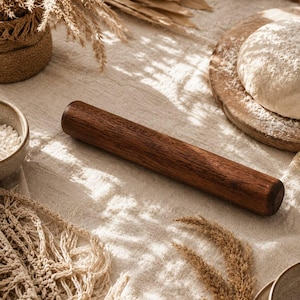 May include: A cylindrical dark brown wooden rolling pin with a smooth, polished finish. The rolling pin features a visible natural wood grain pattern and rounded ends, positioned diagonally across the center of the frame.