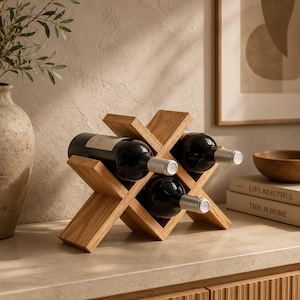 May include: A light brown wooden wine rack with an X-shaped frame holding three dark glass wine bottles with silver foil caps. The rack is constructed from intersecting wooden planks, providing individual slots for each bottle in a horizontal position.