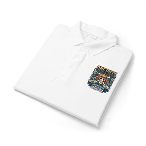 Op de afbeelding: Een wit poloshirt met een afbeelding op de linkerborst. Het ontwerp bevat de tekst ONE PIECE, STRAW HAT PIRATES en Japanse karakters, gecentreerd rond een schedel met een strooien hoed, omringd door blauwe golven en wolken.