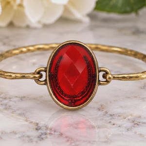 Red faceted oval brass bangle bracelet with horseshoe motif, antiqued gold tone