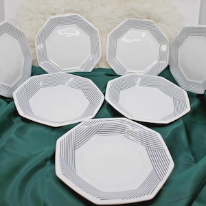 May include: A set of seven white octagonal plates featuring a geometric pattern of thin, dark gray parallel lines arranged in a radiating, angular design along the edges of each plate, creating a consistent visual motif across the entire collection.