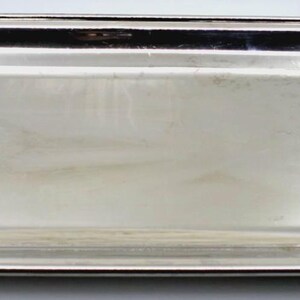 May include: A rectangular silver-toned serving tray with a polished, reflective metallic surface. The tray features slightly curved, raised edges and a smooth, flat base, presenting a clean and uniform appearance throughout the entire object.