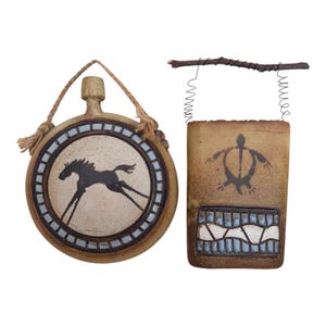 May include: A round tan ceramic canteen with a black horse illustration and a rectangular tan ceramic wall pocket featuring a black turtle graphic. Both items have textured surfaces, blue and white tile-like accents, and hanging hardware.