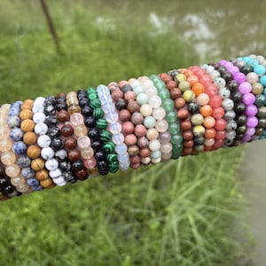 May include: A collection of multiple stretch bracelets featuring round, polished gemstone beads in a wide variety of colours including pink, green, black, blue, white, brown, malachite green, translucent white, and bright turquoise.