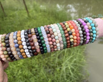 May include: A collection of multiple stretch bracelets featuring round, polished gemstone beads in a wide variety of colours including pink, green, black, blue, white, brown, malachite green, translucent white, and bright turquoise.