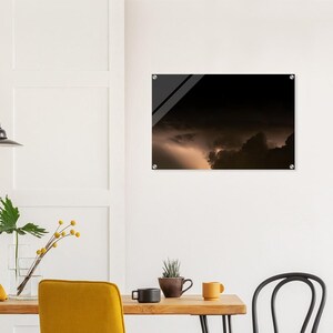 Puede incluir: Un cuadro rectangular de acrílico para pared que muestra un cielo nocturno oscuro y dramático lleno de densas nubes de tormenta y un brillante rayo dorado que ilumina el horizonte, montado con cuatro soportes circulares plateados.