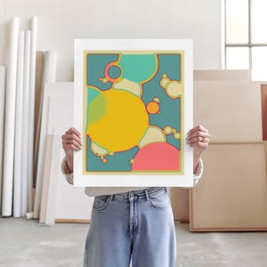 A person is holding up a colorful abstract painting in an art studio.