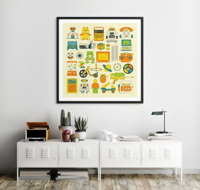 a framed collage of various colorful and whimsical illustrations, including toys, robots, and other playful objects, displayed on a wall above a white cabinet with drawers.