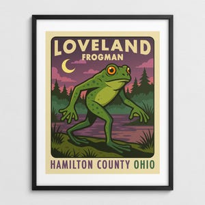 May include: A framed poster featuring a green frog-like creature with orange eyes, labeled "LOVELAND FROGMAN" and "HAMILTON COUNTY OHIO." The background includes a purple sky, a crescent moon, and a forest scene, creating a vintage travel poster aesthetic.