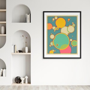 a vibrant abstract painting with a mix of yellow, green, and pink circles and shapes, hanging on a white wall above a shelf with decorative items.