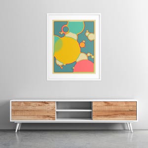 a modern, minimalist living room setting with a white entertainment center and a framed abstract art piece hanging on the wall above it.
