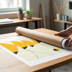 A person is rolling up a large roll of paper to create a framed artwork on a wooden table.