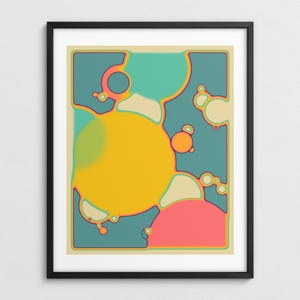 The image is a framed abstract artwork with a vibrant color scheme of yellow, pink, blue, and green. The artwork features various shapes and forms, including circles, ovals, and other organic and geometric elements, creating a visually striking and dynamic composition.