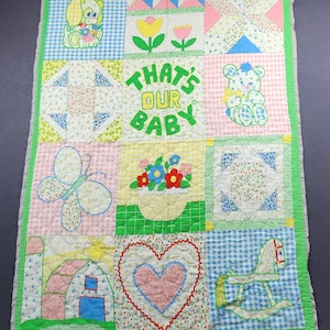 Könnte beinhalten: Eine rechteckige Patchwork-Decke mit zwölf Quadraten und verschiedenen Applikationen, darunter ein Welpe, Blumen, ein Schmetterling, eine Scheune, ein Herz und ein Schaukelpferd. Das mittlere Quadrat zeigt den grünen Text THAT'S OUR BABY.
