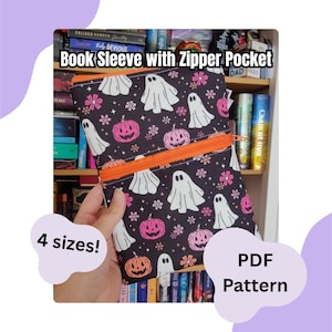 Puede incluir: Una funda de tela negra para libros con un patrón repetitivo de fantasmas blancos, calabazas rosas y flores pequeñas. La funda incluye un bolsillo horizontal con cremallera naranja en la parte delantera. El texto dice Book Sleeve with Zipper Pocket, 4 sizes!, y PDF Pattern.