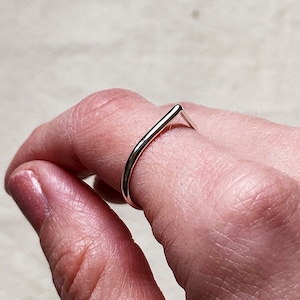 Op de afbeelding: Een zilveren ring met een eenvoudig, gebogen ontwerp. De ring wordt aan een vinger gedragen.