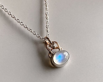May include: A silver chain necklace with a delicate pendant featuring a round, iridescent moonstone set in a silver and gold setting.