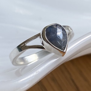 May include: A silver ring with a pear-shaped blue gemstone.