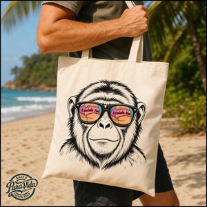 Peut inclure: Un sac fourre-tout en toile beige avec une illustration en noir et blanc d'un chimpanzé portant des lunettes de soleil noires. Les verres des lunettes reflètent un bas de bikini rose avec le texte A cachete Mas imprimé sur le tissu.