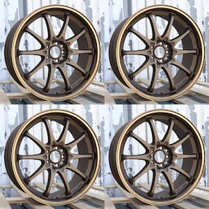 May include: A set of four bronze-colored metal car wheels, each featuring a multi-spoke design with a central hub and a circular rim. The wheels have a matte finish and are arranged in a grid pattern, showcasing the intricate spoke structure.