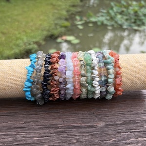 May include: A collection of eleven stretch bracelets made from small, irregular tumbled gemstone chips in a variety of colors including turquoise, black, brown, purple, light blue, pink, green, white, and orange, arranged side by side.