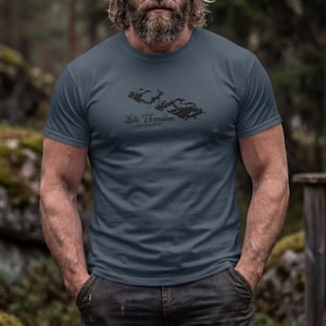 May include: A slate blue short-sleeved t-shirt featuring a black graphic of the Lake Vermilion map outline centered on the chest, with the text Lake Vermilion printed in a cursive script directly below the map graphic.