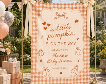 May include: A rectangular fabric banner with an orange and white gingham pattern, featuring the text 'a little pumpkin IS ON THE WAY WELCOME TO Olivia's Baby Shower OCTOBER 15, 20xx' and illustrations of pumpkins, hearts, and leaves.
