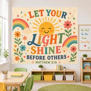 May include: A rectangular wall tapestry featuring a cream background with a central yellow smiling sun. The text reads LET YOUR LIGHT SHINE BEFORE OTHERS MATTHEW 5:16 in colorful letters. The design includes rainbows, flowers, and stars.