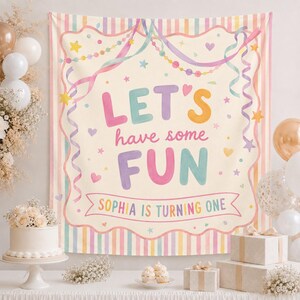May include: A rectangular party backdrop featuring a cream-colored center with the text "LET'S have some FUN" in colorful letters and "SOPHIA IS TURNING ONE" on a banner. The border has pastel vertical stripes, ribbons, stars, and hearts.