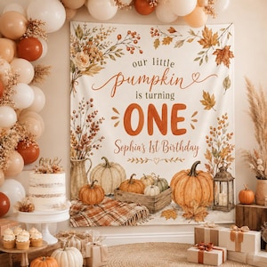 May include: A rectangular fabric backdrop featuring autumn-themed illustrations of pumpkins, dried foliage, and a lantern. The text reads: our little pumpkin is turning ONE Sophia's 1st Birthday. The color palette includes shades of orange, cream, and brown.