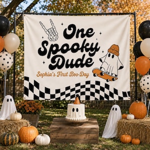 Peut inclure: Une toile de fond rectangulaire blanc cassé avec le texte noir One Spooky Dude et Sophia's First Boo-Day. Le motif comprend une main squelette, un fantôme portant un bonnet orange sur un skateboard et une bordure à damier noir et blanc.