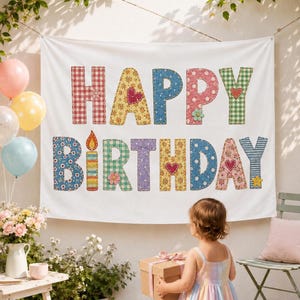 May include: A white fabric banner featuring the text HAPPY BIRTHDAY in large, multi-colored, patterned letters. Each letter displays distinct designs including gingham, floral, and polka dot prints, accented with small heart and flower motifs.