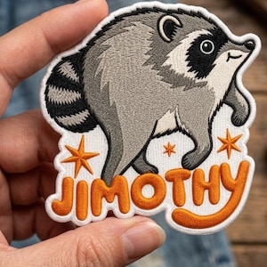 May include: An embroidered patch featuring a gray and black raccoon with a striped tail, positioned above the orange text JIMOTHY. The design includes three orange star accents on a white background with a thick white border around the edges.