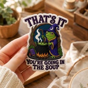 May include: An embroidered patch featuring a green frog wearing a purple wizard hat and robe, stirring a black cauldron over a fire. The text reads THAT'S IT YOU'RE GOING IN THE SOUP. The design includes a purple book and a tree background.