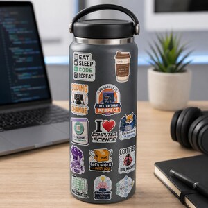 K&ouml;nnte beinhalten: Eine dunkelgraue Edelstahl-Trinkflasche mit schwarzem Deckel und Tragegriff, beklebt mit verschiedenen bunten Aufklebern zu Informatik-Themen, Programmier-Witzen und Technik-Grafiken, darunter Texte wie Eat Sleep Code Repeat und I Love Computer Science.