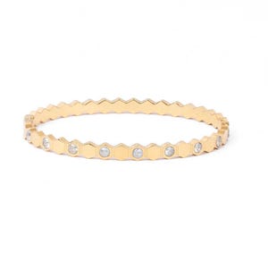 May include: A gold-toned bangle bracelet featuring a repeating geometric hexagonal pattern along the band. The design alternates between smooth, solid gold-coloured hexagonal segments and segments set with small, clear, round, sparkling stones.