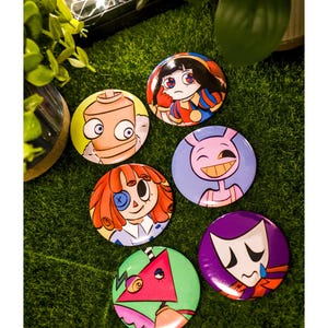 Pode incluir: Seis botões redondos com ilustrações coloridas de desenhos animados. Os designs incluem um personagem bege, uma figura de cabelo escuro, uma criatura roxa, um personagem ruivo com um tapa-olho, um triângulo verde e uma máscara triste.