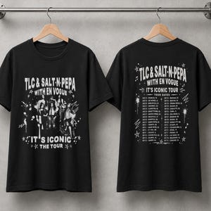 Op de afbeelding: Een zwart t-shirt met korte mouwen en een witte grafische print van TLC, Salt-N-Pepa en En Vogue op de voorkant met de tekst "TLC & SALT-N-PEPA WITH EN VOGUE IT'S ICONIC THE TOUR". De achterkant toont een lijst met tourdata en locaties.