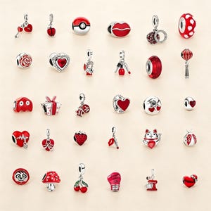 May include: A collection of thirty silver-toned jewelry charms featuring red enamel and crystal accents. The assortment includes various shapes such as hearts, flowers, animals, food items, and symbolic objects, all designed for attachment to bracelets.