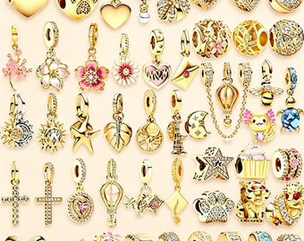 May include: A collection of gold-toned jewellery charms featuring various designs including hearts, flowers, animals, stars, crosses, and geometric shapes, many accented with clear crystals, pink enamel, or blue stones, arranged in a grid pattern.
