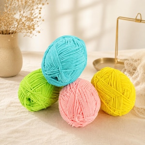 May include: Four round skeins of soft, plush yarn in bright colours. The collection includes one turquoise blue, one lime green, one pastel pink, and one vibrant yellow ball of yarn, each featuring a thick, velvety texture and a consistent twist.