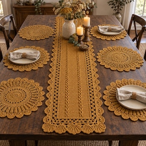 May include: A mustard yellow crochet table runner and four matching round placemats with scalloped edges. The runner features a central cable knit pattern. Four white ceramic plates with beige linen napkins and wooden napkin rings are set on the table.