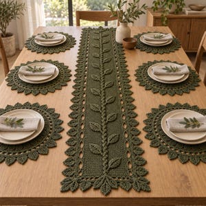 May include: A dark olive green crochet table runner featuring a central vine pattern with leaves, bordered by a decorative leaf edge. The set includes six matching round crochet placemats, each topped with a white plate and a linen napkin.