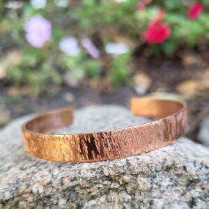 May include: A copper bracelet with a hammered texture. The bracelet is a simple design and has a shiny finish.