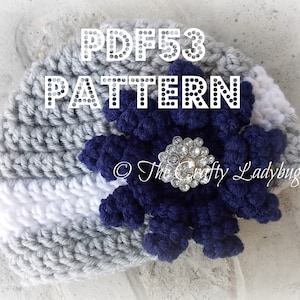 May include: A gray and white crocheted baby hat with a navy blue flower and a rhinestone embellishment. The hat is labeled "PDF53 PATTERN" and "The Crafty Ladybug".
